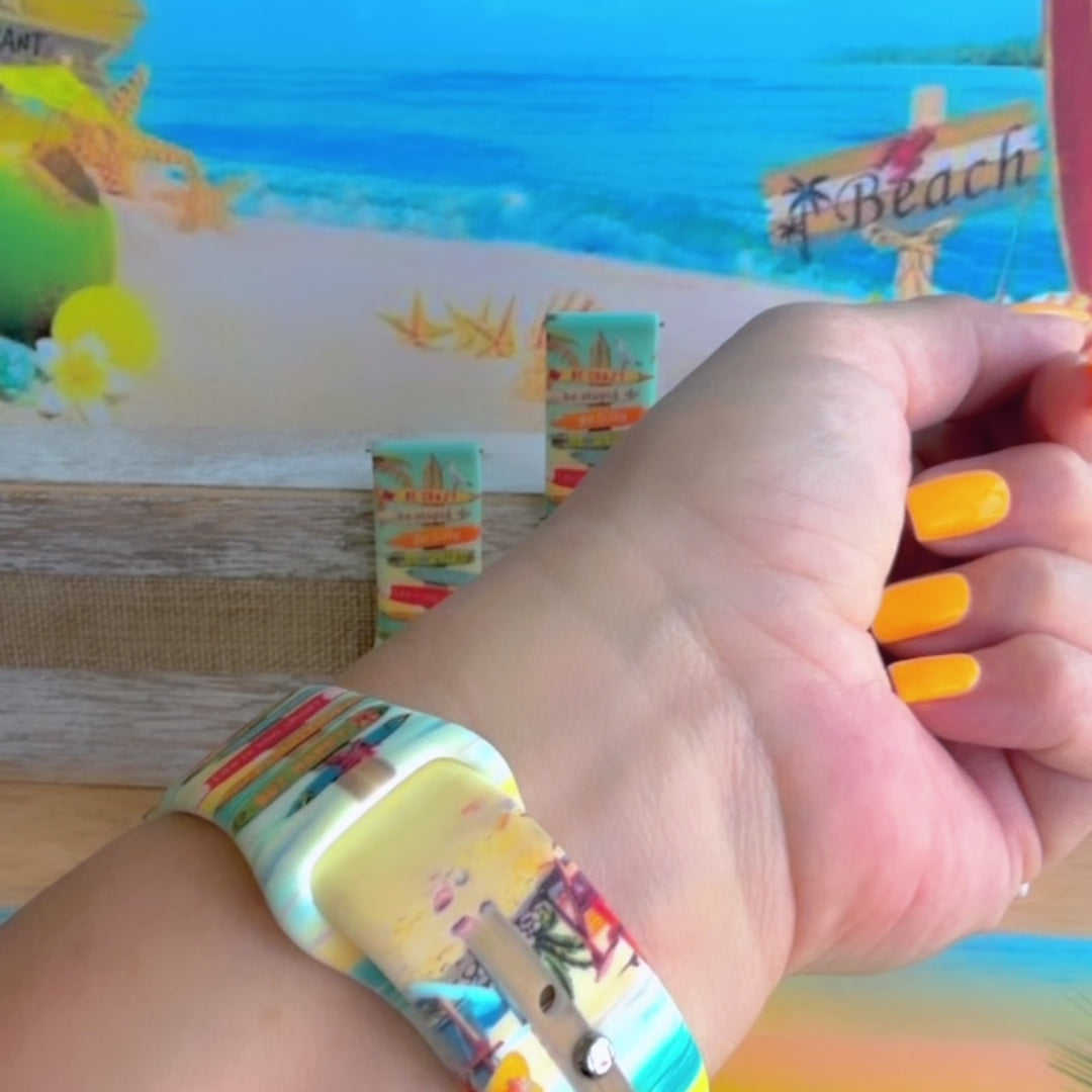 Seaside State of Mind silicone Samsung Watch band with colorful surfboard signpost on a beach scene and "Be Crazy, Be Silly, Be Weird—life is too short to be anything but happy" message, shown displayed and worn on Apple Watch against a beach backdrop.
