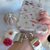 Video of the Fall Floral Bliss scrunchie phone wrist strap showing the cream fabric with rust and olive watercolor autumn florals, the silver clasp, and how it attaches to a phone case.