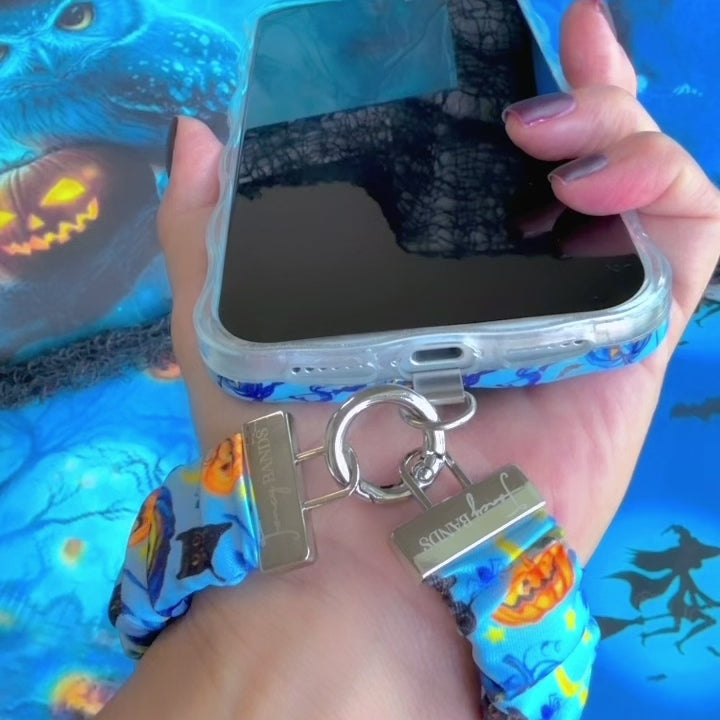 Video of The Bewitching Hour Scrunchie Phone Wrist Strap being clipped to a phone case and worn on the wrist, showing the gathered blue witch print fabric and metal clasp.