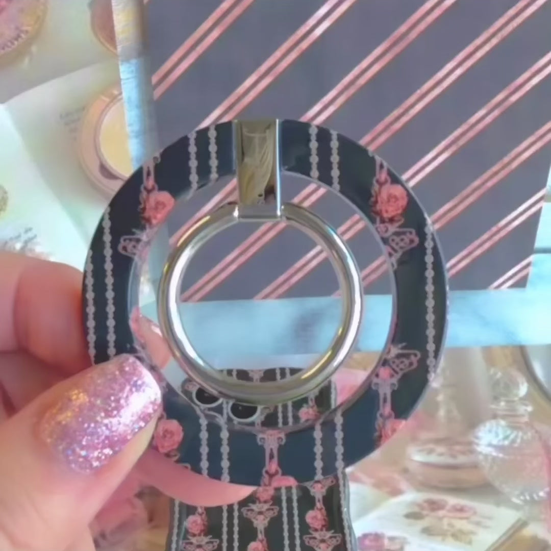 Video of a hand placing the Pretty Little Details pearl and rose MagSafe grip ring on the back of the matching iPhone case and rotating the silver ring.