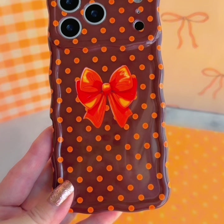Video of the Spotted Looking Cute Wavy Luxe MagSafe iPhone case showing the glossy chocolate brown finish, pumpkin-orange polka dots, and orange bow from every angle.