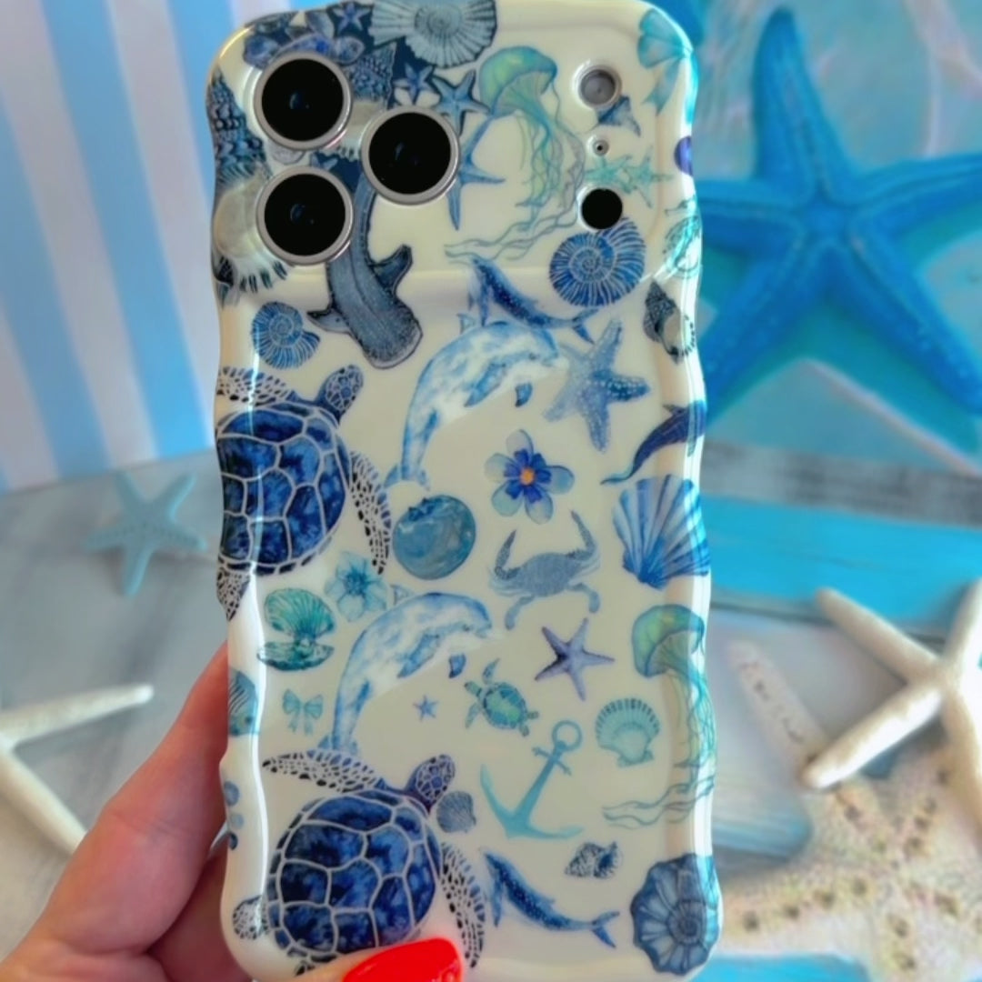 Trendy white wavy iPhone case featuring a blue monochrome collage of sea turtles, whales, dolphins, and starfish with a high-gloss finish.
