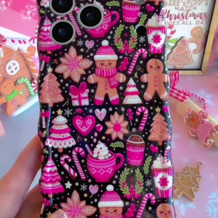 Video: close-up of the Merry Mugs & Ginger Hugs Wavy Luxe MagSafe iPhone case in hand showing the glossy pink gingerbread and cocoa mug print on black and wavy edges