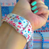 Party In The USA silicone Apple Watch band with fireworks, balloons, cupcakes, flag bunting, and stars in red, white, and blue on a cream base, shown displayed and worn on Apple Watch against a patriotic 4th of July backdrop.