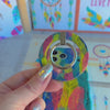 Rainbow Feather Muse pattern MagSafe phone grip ring with vibrant overlapping yellow coral and navy feathers compatible with iPhone and Samsung