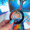The Wishing Tree mystical fantasy MagSafe phone grip ring with vibrant orange and blue swirling filigree branches on a dark background compatible with iPhone and Samsung