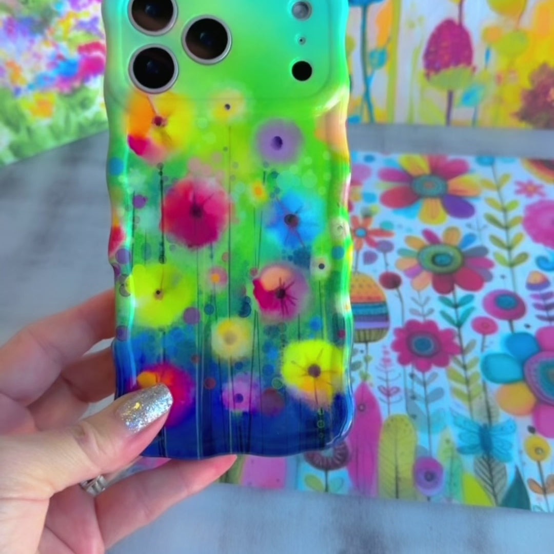 Wavy iPhone case featuring vibrant watercolor flowers in pink, red, yellow, and orange on a green and blue gradient background.