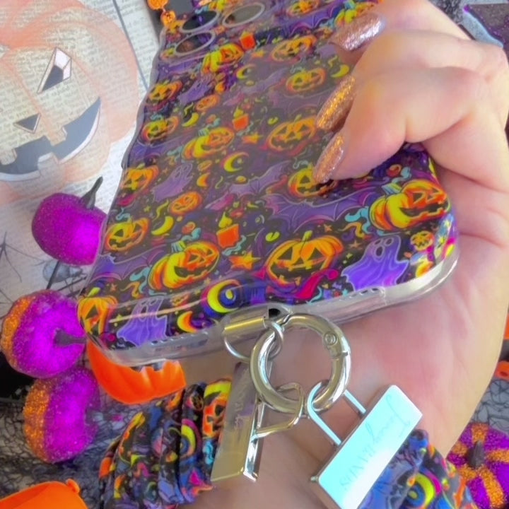 Video of the Jack-O-Lantern Jive scrunchie phone wrist strap clipped to the matching case and worn on the wrist, showing the violet neon pumpkin print.