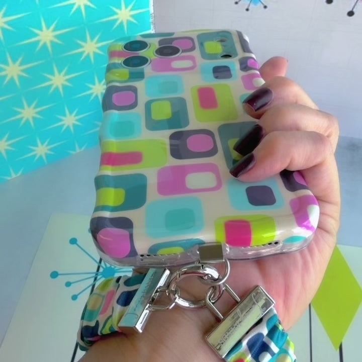 Video of the Mod Mood Scrunchie Phone Wrist Strap clipped to the matching case and worn on the wrist, showing the gathered turquoise, lime and pink geometric fabric and metal clasp.