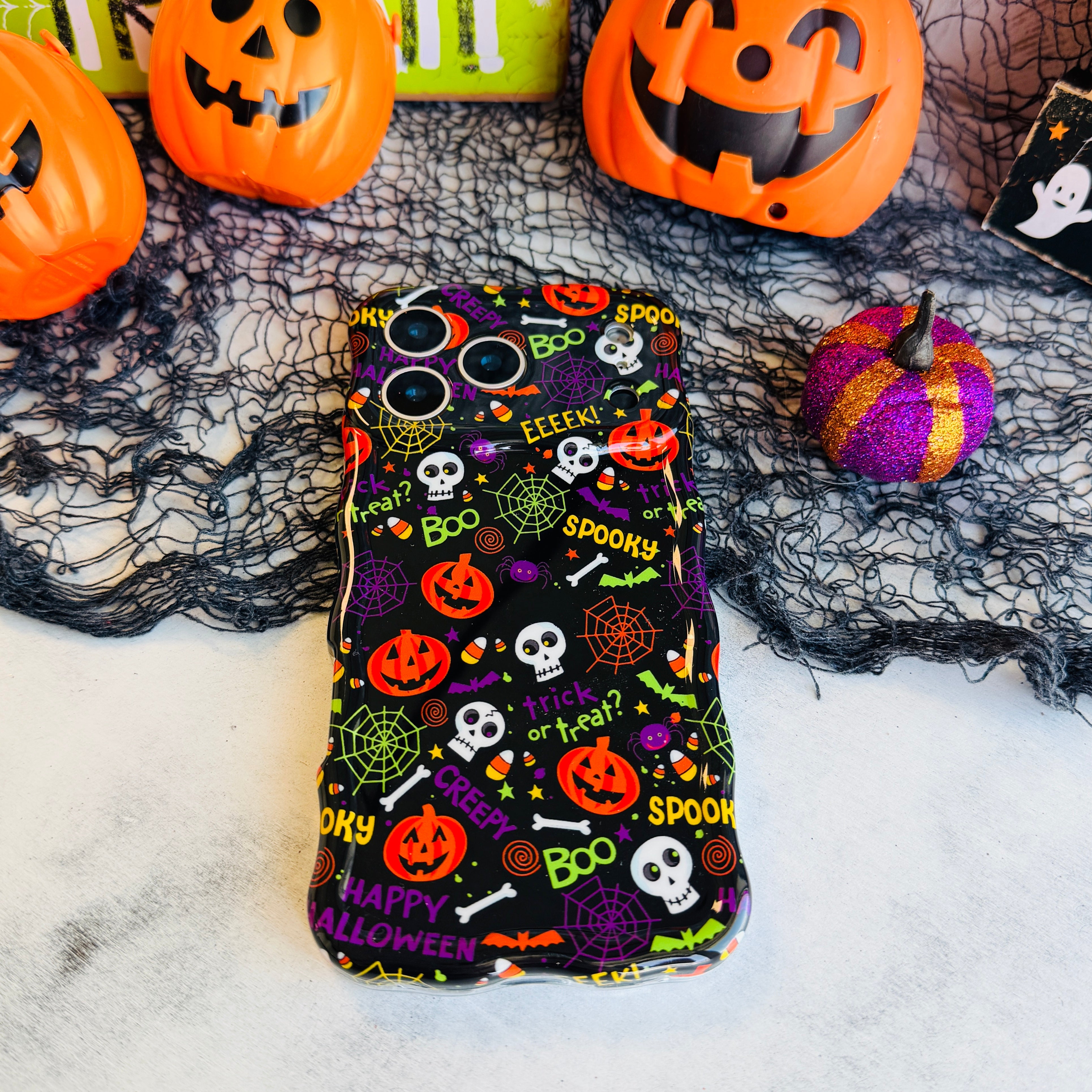 Spooky Wavy Luxe MagSafe iPhone case laid flat on black spiderweb mesh with an orange jack-o-lantern pail and felt pumpkins